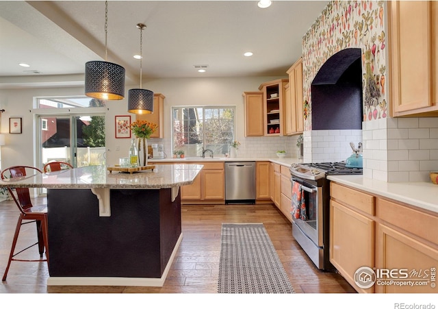 kitchen with appliances with stainless steel finishes, a kitchen bar, light brown cabinets, hanging light fixtures, and hardwood / wood-style floors