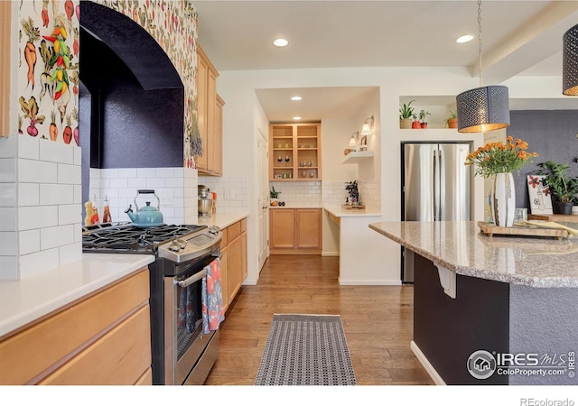 kitchen with stainless steel appliances, tasteful backsplash, light brown cabinets, light wood-type flooring, and decorative light fixtures