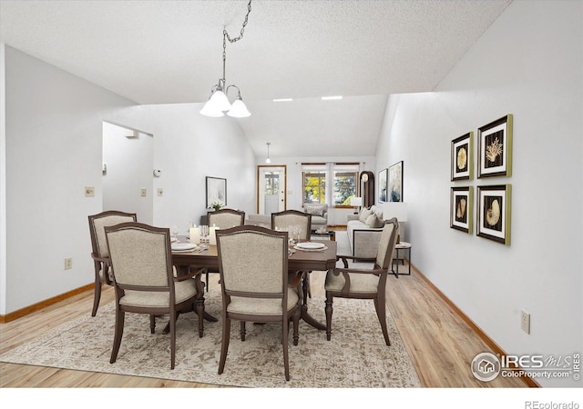 dining area featuring light hardwood / wood-style floors, a notable chandelier, a textured ceiling, and vaulted ceiling