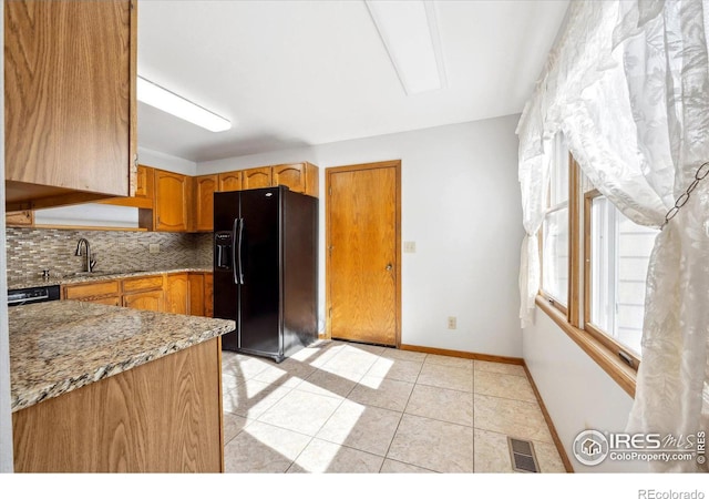 kitchen with light stone counters, light tile patterned floors, sink, black fridge with ice dispenser, and backsplash