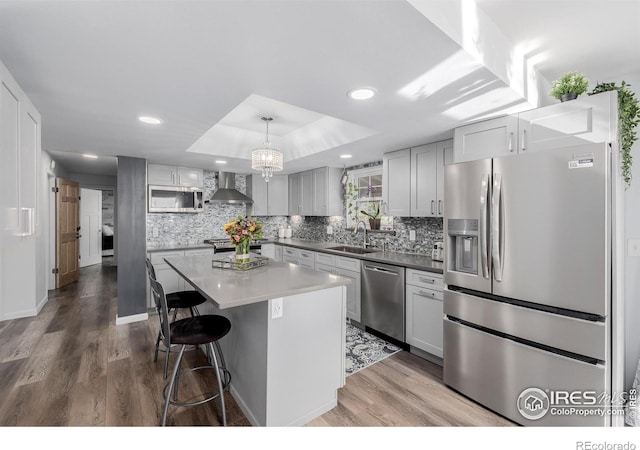 kitchen featuring stainless steel appliances, a kitchen island, wall chimney range hood, hanging light fixtures, and hardwood / wood-style flooring