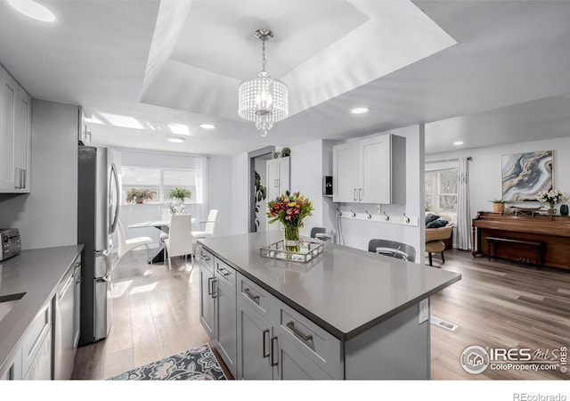 kitchen with stainless steel appliances, a tray ceiling, hanging light fixtures, light hardwood / wood-style flooring, and a center island