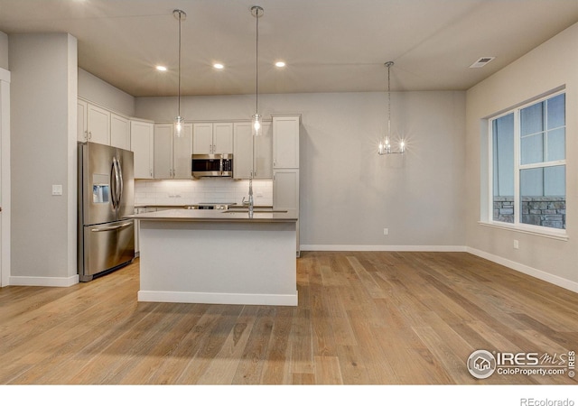 kitchen with light hardwood / wood-style floors, white cabinets, hanging light fixtures, an island with sink, and appliances with stainless steel finishes