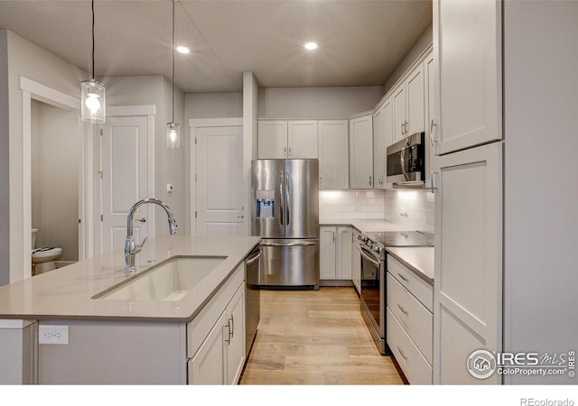 kitchen featuring a center island with sink, appliances with stainless steel finishes, hanging light fixtures, sink, and white cabinets