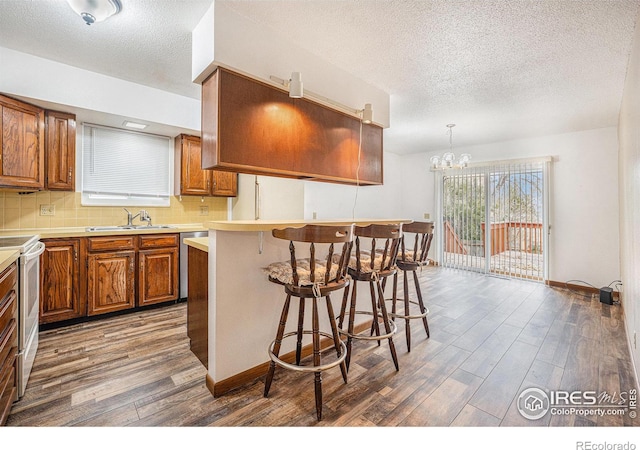 kitchen featuring sink, a kitchen breakfast bar, dark hardwood / wood-style floors, pendant lighting, and white electric stove