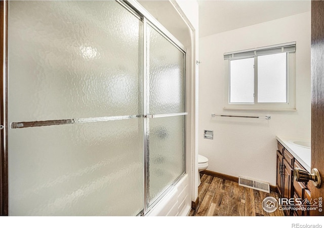 full bathroom with toilet, vanity, hardwood / wood-style flooring, and combined bath / shower with glass door