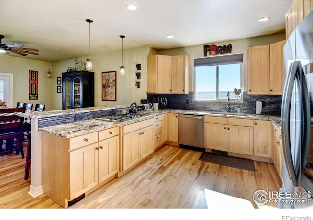 kitchen with stainless steel appliances, light brown cabinetry, light hardwood / wood-style floors, a breakfast bar area, and kitchen peninsula