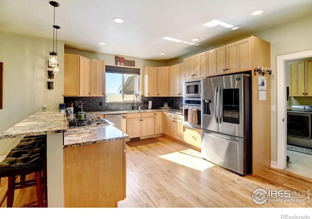 kitchen with stainless steel appliances, light wood-type flooring, decorative light fixtures, a breakfast bar, and kitchen peninsula