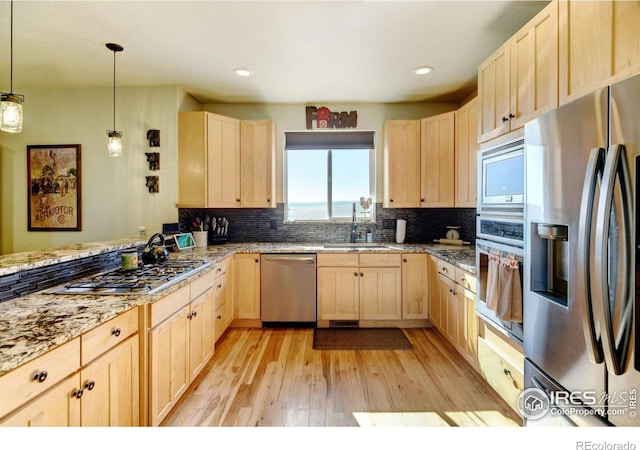 kitchen with pendant lighting, sink, light brown cabinets, light wood-type flooring, and appliances with stainless steel finishes