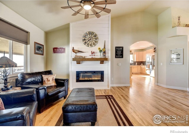 living room featuring light wood-type flooring, a fireplace, ceiling fan, and vaulted ceiling