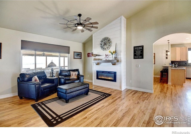 living room featuring high vaulted ceiling, a large fireplace, ceiling fan, and light wood-type flooring