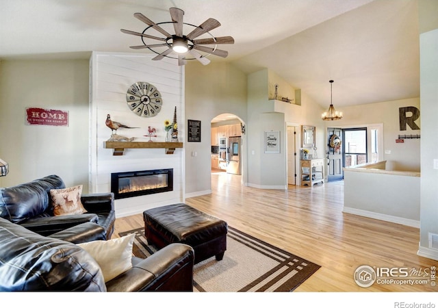 living room featuring high vaulted ceiling, light wood-type flooring, a large fireplace, and ceiling fan with notable chandelier