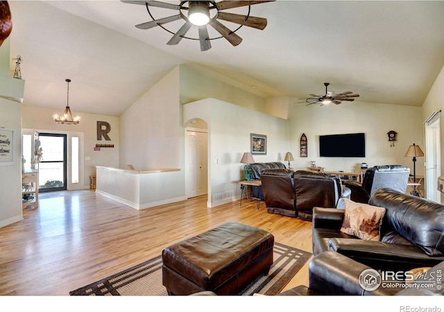 living room with light wood-type flooring, ceiling fan with notable chandelier, and high vaulted ceiling