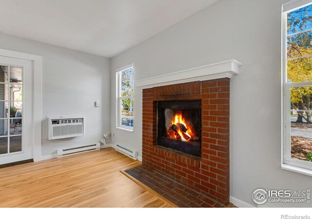 unfurnished living room featuring a brick fireplace, an AC wall unit, hardwood / wood-style floors, and a baseboard heating unit