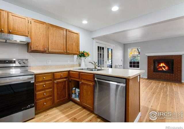 kitchen featuring appliances with stainless steel finishes, light wood-type flooring, kitchen peninsula, a brick fireplace, and sink