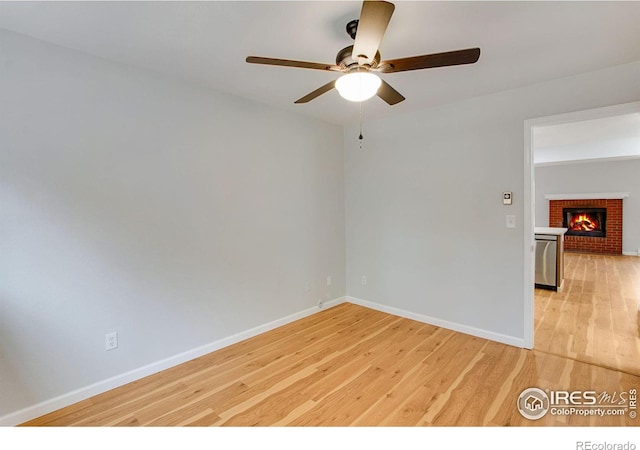 empty room featuring a fireplace, ceiling fan, and light hardwood / wood-style floors