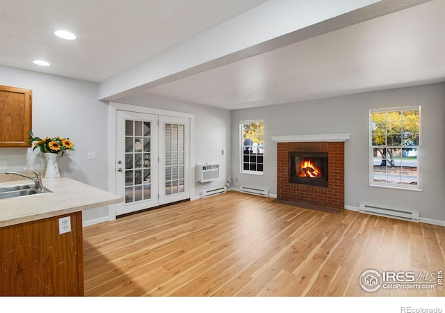 unfurnished living room with a wall unit AC, light hardwood / wood-style floors, a brick fireplace, a baseboard heating unit, and sink