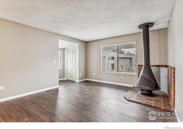 unfurnished room featuring a wood stove, dark wood-type flooring, and a textured ceiling