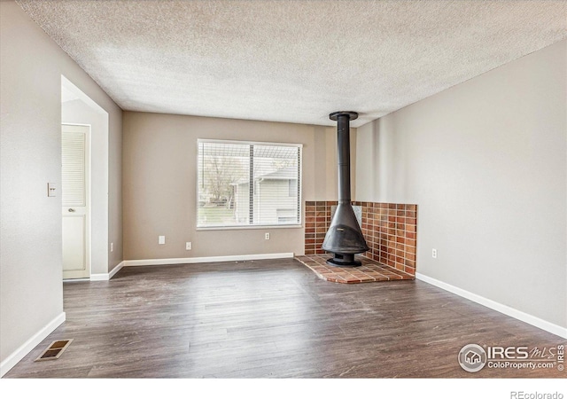 unfurnished living room featuring a wood stove, dark hardwood / wood-style floors, and a textured ceiling