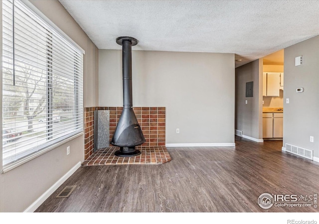 unfurnished living room featuring dark hardwood / wood-style flooring, a wood stove, and a textured ceiling