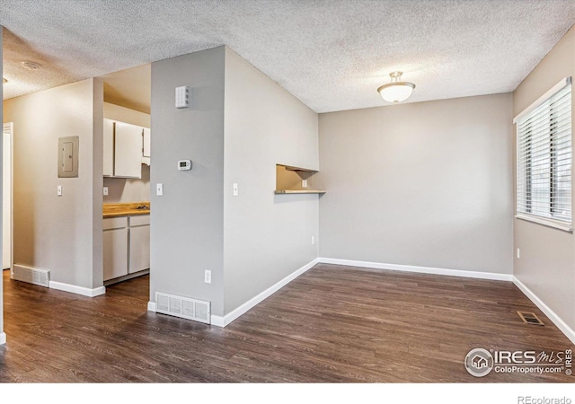 empty room featuring dark wood-type flooring, electric panel, and a textured ceiling