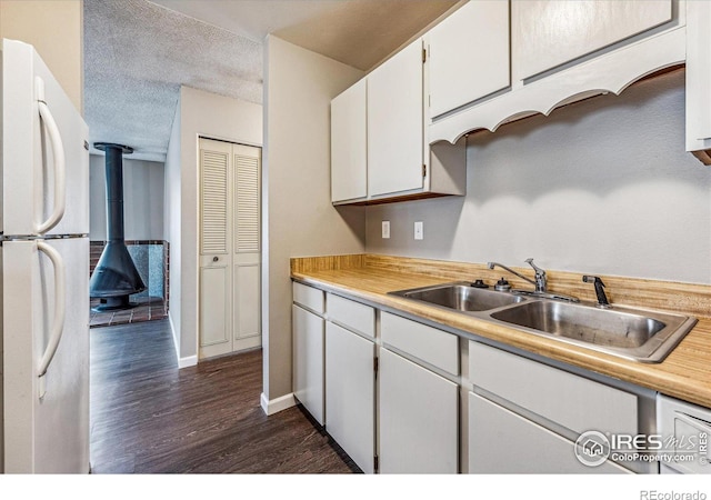 kitchen with white cabinetry, sink, a wood stove, dark wood-type flooring, and white refrigerator