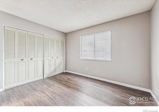 unfurnished bedroom featuring a textured ceiling, a closet, and light hardwood / wood-style flooring