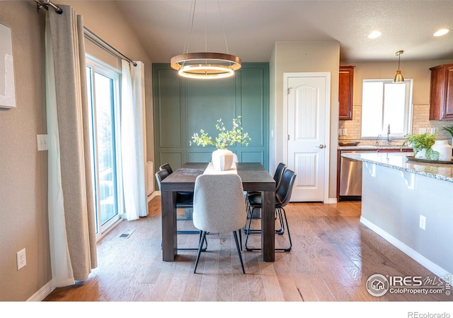 dining room featuring sink, a chandelier, vaulted ceiling, and light hardwood / wood-style flooring