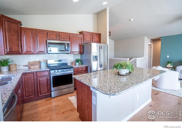 kitchen with a center island, vaulted ceiling, decorative backsplash, light wood-type flooring, and appliances with stainless steel finishes