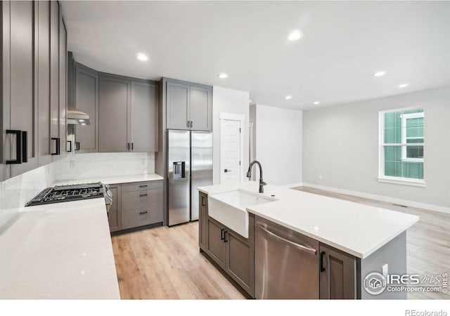 kitchen with light hardwood / wood-style floors, stainless steel appliances, sink, an island with sink, and range hood