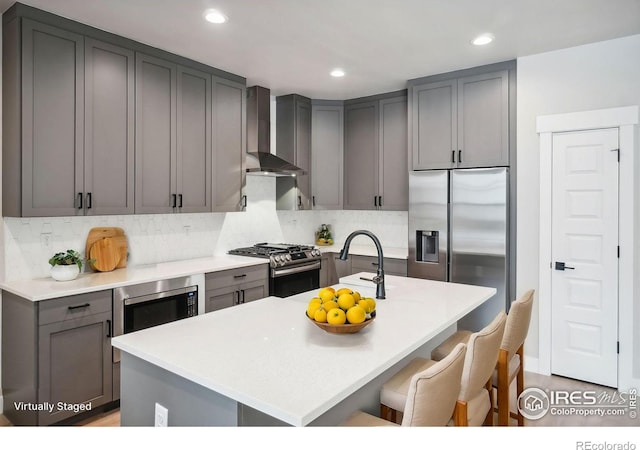 kitchen featuring an island with sink, tasteful backsplash, wall chimney exhaust hood, and stainless steel appliances