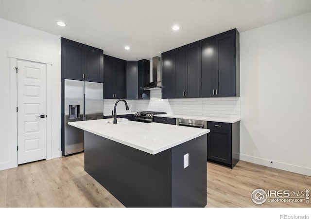 kitchen with an island with sink, light hardwood / wood-style flooring, wall chimney exhaust hood, and stainless steel appliances