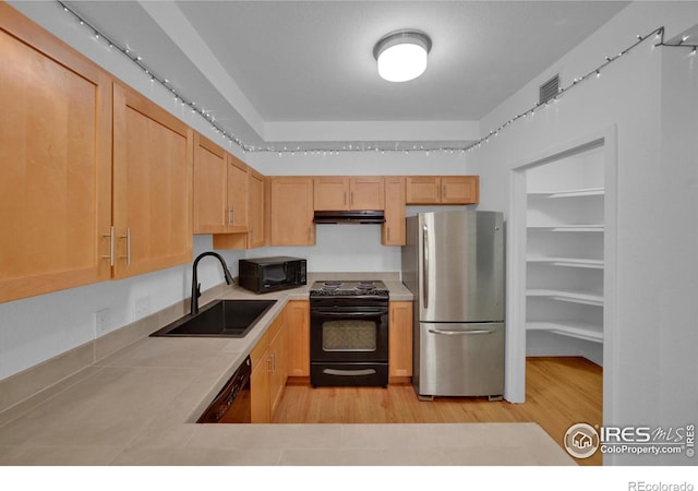 kitchen with light brown cabinetry, sink, black appliances, and light hardwood / wood-style floors