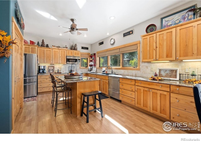 kitchen featuring light hardwood / wood-style floors, light stone counters, a kitchen breakfast bar, a kitchen island, and appliances with stainless steel finishes