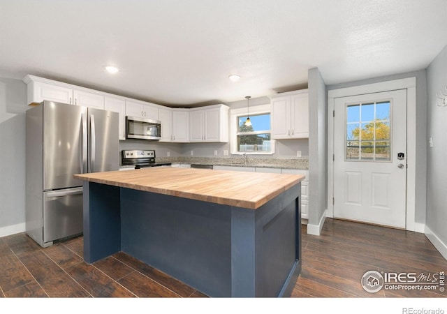 kitchen with white cabinets, butcher block counters, a kitchen island, appliances with stainless steel finishes, and hanging light fixtures