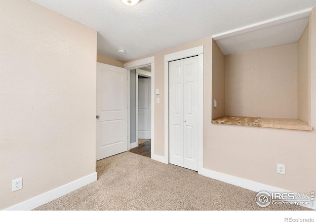 unfurnished bedroom with a textured ceiling, carpet floors, a closet, and baseboards