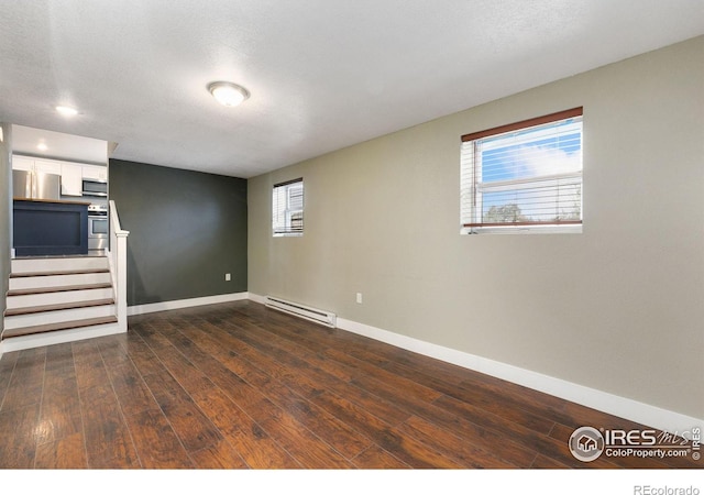 unfurnished living room with dark wood-style floors, baseboard heating, a textured ceiling, baseboards, and stairs