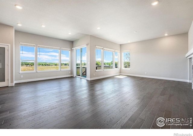 unfurnished living room with a textured ceiling, a healthy amount of sunlight, and dark wood-type flooring