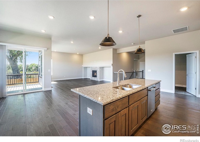 kitchen featuring sink, light stone counters, dark hardwood / wood-style floors, pendant lighting, and a center island with sink