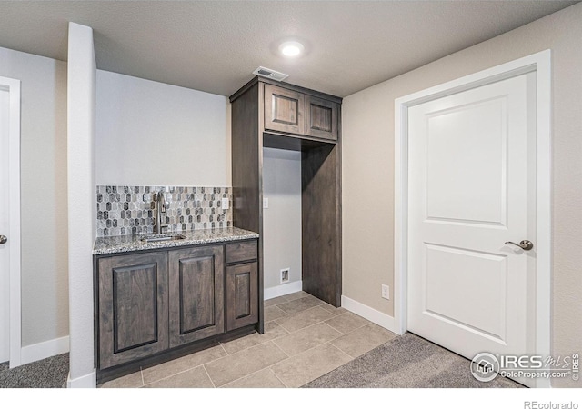 kitchen featuring backsplash, light stone counters, dark brown cabinetry, sink, and light tile patterned floors