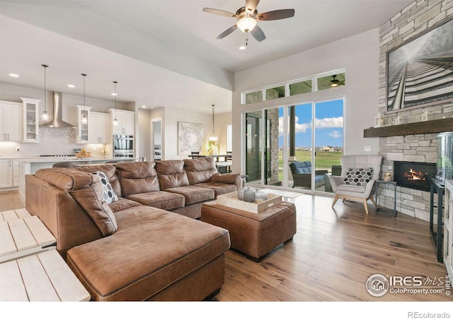 living room with a stone fireplace, ceiling fan with notable chandelier, light hardwood / wood-style floors, and a high ceiling