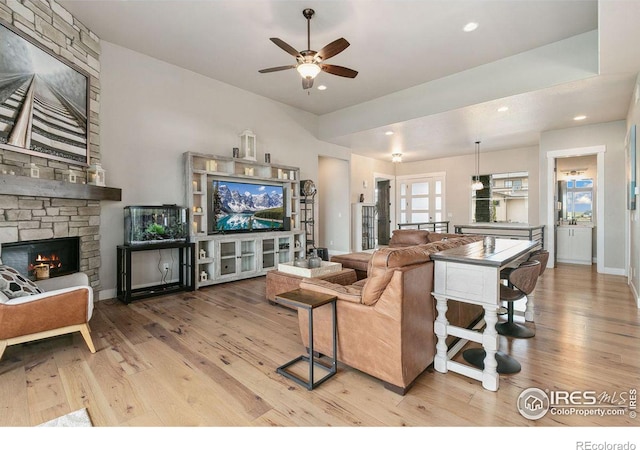 living room featuring ceiling fan, a stone fireplace, and light hardwood / wood-style flooring