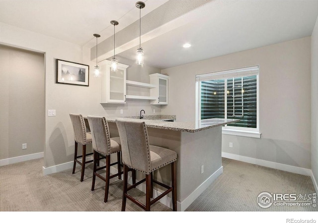 kitchen featuring light carpet, pendant lighting, a breakfast bar, white cabinets, and kitchen peninsula