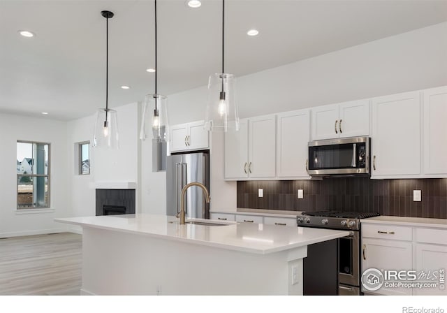 kitchen with a center island with sink, appliances with stainless steel finishes, sink, decorative light fixtures, and white cabinets