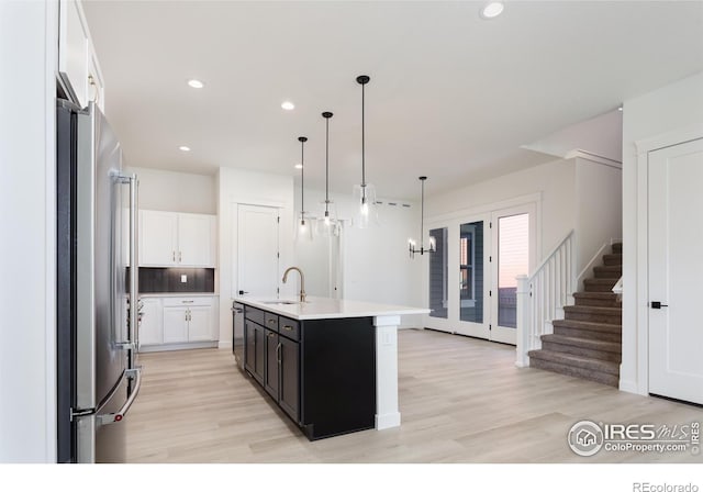 kitchen with a center island with sink, stainless steel appliances, pendant lighting, sink, and white cabinetry