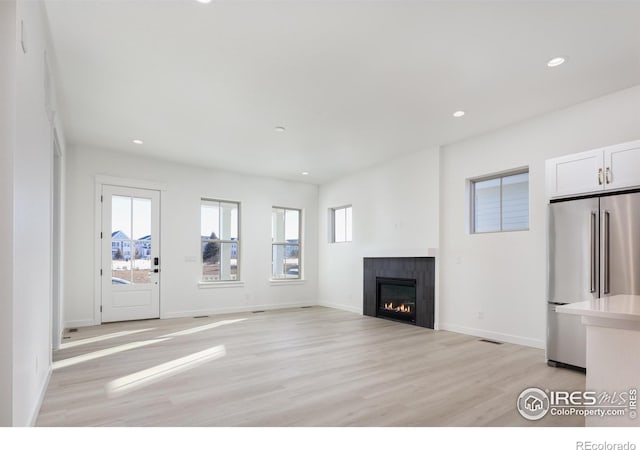 unfurnished living room featuring a tiled fireplace, light hardwood / wood-style floors, and a healthy amount of sunlight