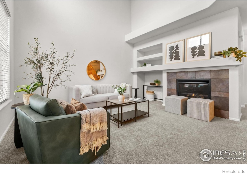 living room with a tile fireplace, built in features, carpet floors, and a healthy amount of sunlight