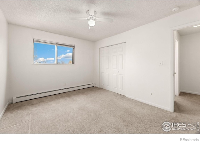 unfurnished bedroom featuring a baseboard heating unit, a textured ceiling, light carpet, ceiling fan, and a closet