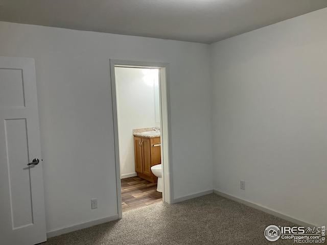 unfurnished bedroom with hardwood / wood-style floors, connected bathroom, and sink