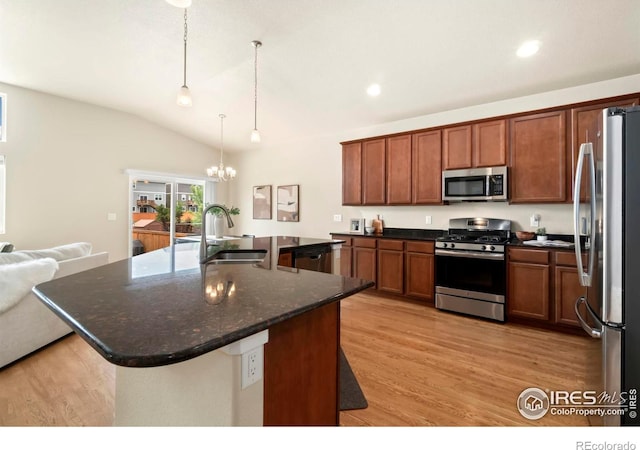 kitchen with stainless steel appliances, vaulted ceiling, an island with sink, light hardwood / wood-style flooring, and decorative light fixtures